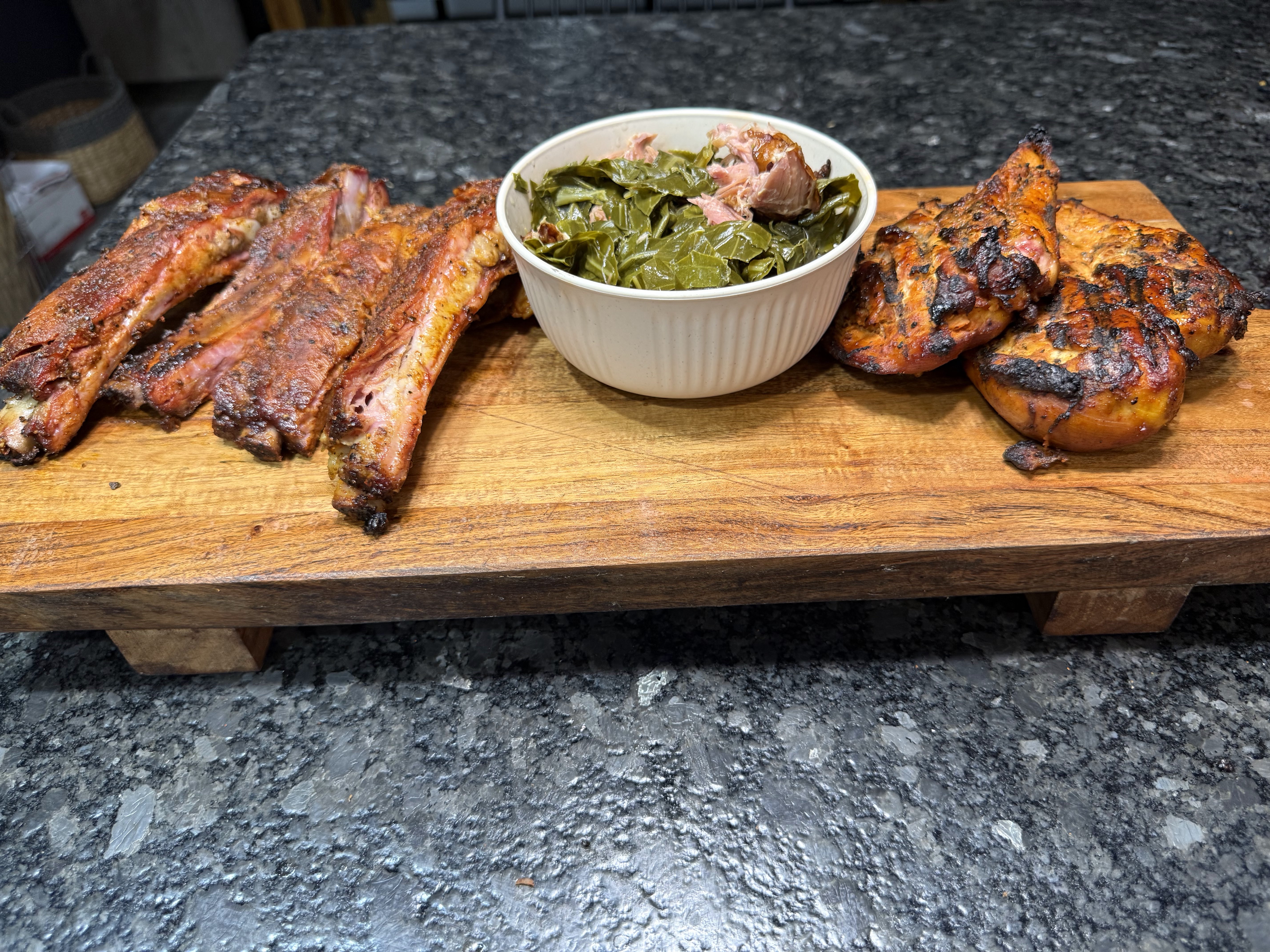 Barbecue ribs, grilled chicken, and collard greens on a serving board