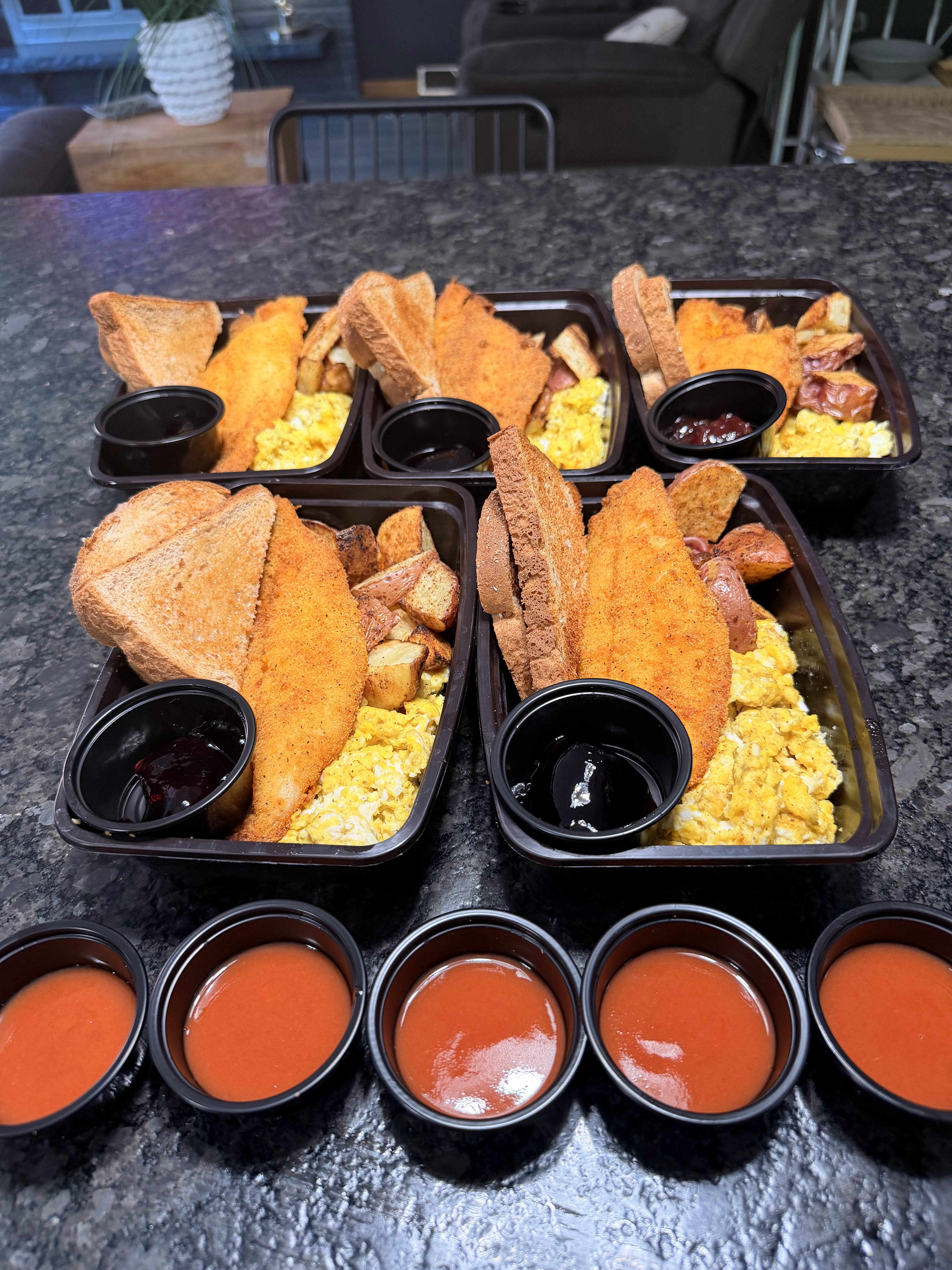 Breakfast meal prep trays with fish, eggs, potatoes, toast, and sauces